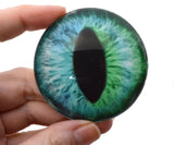 Glass eye with green and blue coloration held in a hand against a white background