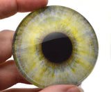 Close-up of a hand holding a glass eye with yellow and green patterns.
