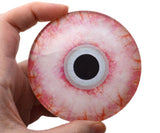 Hand holding a large glass eye with a pink and orange pattern and a black center.