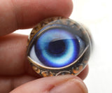 Close-up of a hand holding a decorative object resembling an eye with intricate detailing.