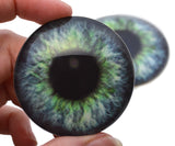 Realistic artificial eye with green and blue iris held by a hand against a white background