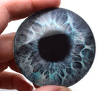 Close-up of a blue and black large glass eye held between fingers